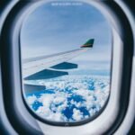 View of an airplane wing above the clouds through a cabin window, for travelers flying with CBD