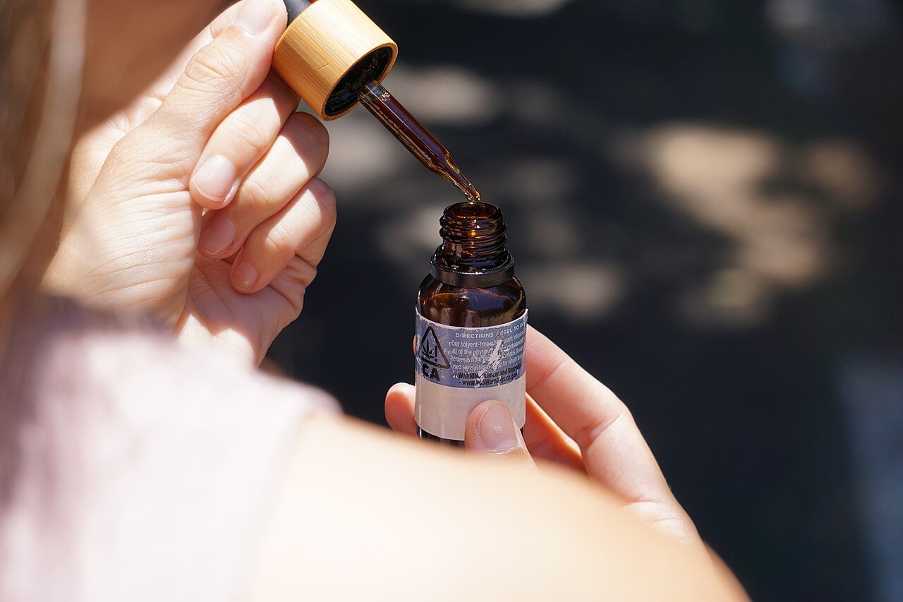 CBD oil dropper bottle held above an open container, used by Danish buyers for daily CBD supplementation