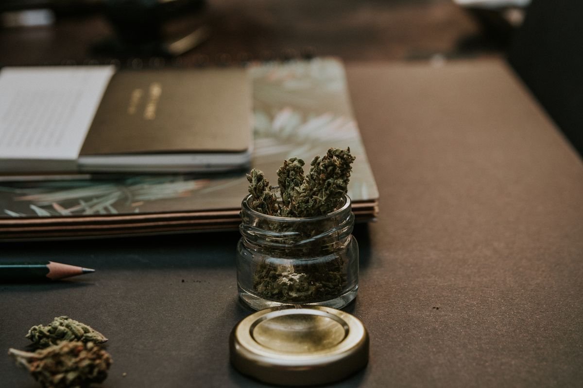 Dried cannabis flower in a small glass jar beside a notebook, Canada regulates CBD as cannabis