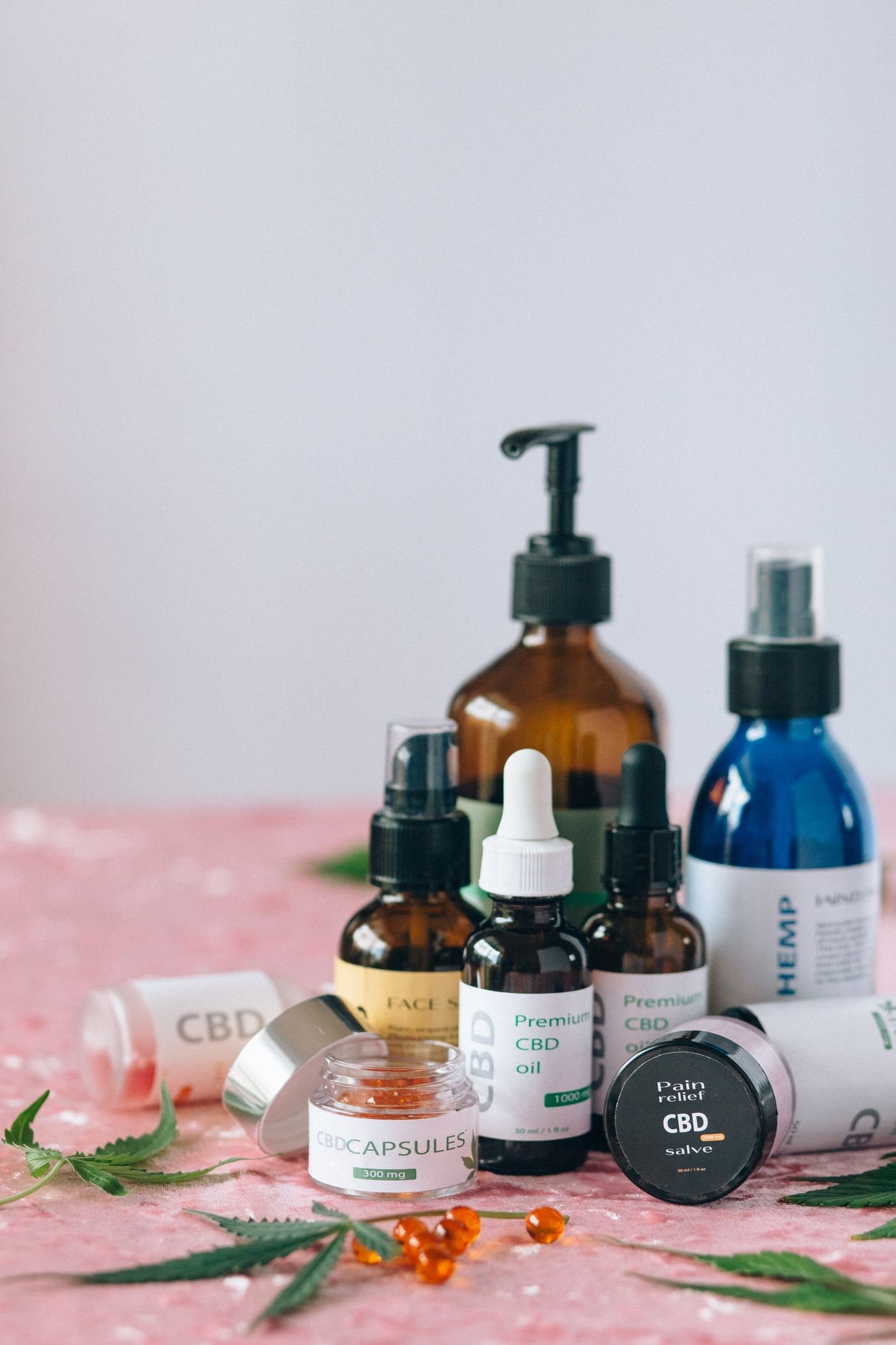 Several CBD oil bottles, capsules and salves next to hemp leaves, showing different CBD product types