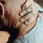 Man holding his sore neck and shoulder, the kind of localised ache a CBD freeze roller is applied to