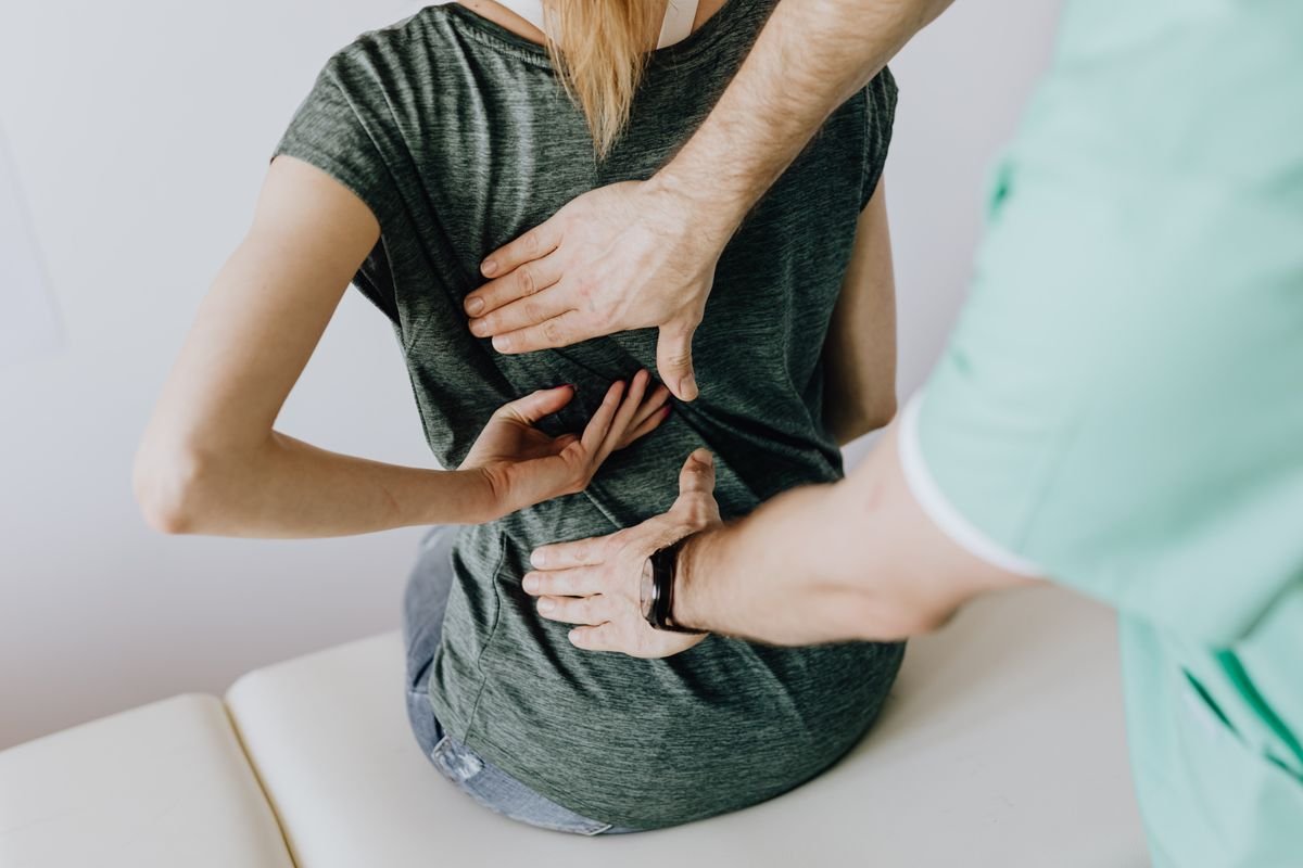 A clinician examining a seated patient's lower back, assessing nerve pain and neuropathy